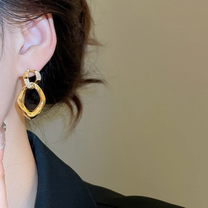Detailed close-up of geometric twisted gold earrings with sparkling zircon inlay on model