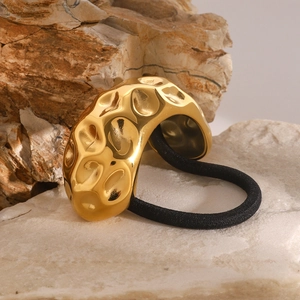 Hammered gold metal hair ring with black elastic band on natural rock background