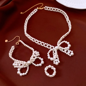 Detailed set of pearl bow necklace and bracelet with gold accents on red fabric