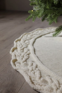 Close-up of cream knitted Christmas tree skirt featuring intricate cable knit patterns
