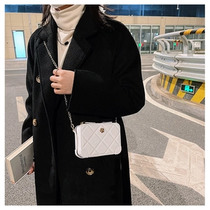 Detail of a white quilted PVC jelly bag with gold chain strap on a black coat