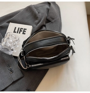 Detail showing triple-zipper compartments and textured black PU leather of the crossbody bag