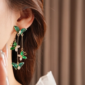 Gros plan de boucles d'oreilles pendantes dorées avec papillons en cristal vert