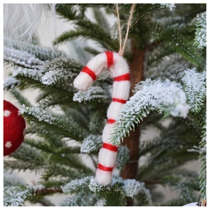 Close-up of red and white striped wool felt candy cane hanging on a snowy pine branch