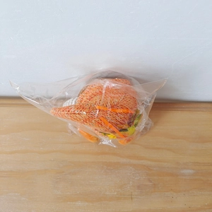 Detail shot of a knitted orange Thanksgiving gnome plush in clear plastic packaging on wood