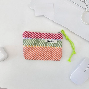 Macro shot of colorful striped woven pouch with a bright neon green zipper pull on a desk
