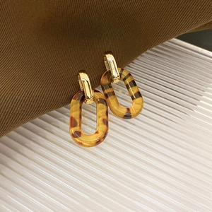 Macro shot of amber leopard resin link earrings with gold clasp on textured fabric
