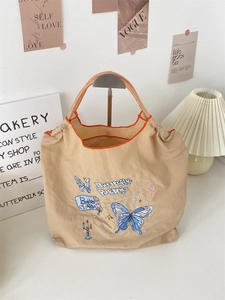Detail showing the blue butterfly embroidery and woven orange rope handle of the tote bag