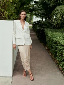 Close-up of beige satin skirt with lace hem paired with a pinstriped blazer in a garden