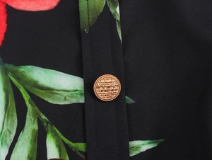 Gros plan sur le bouton doré texturé d'une robe plissée à imprimé floral rouge