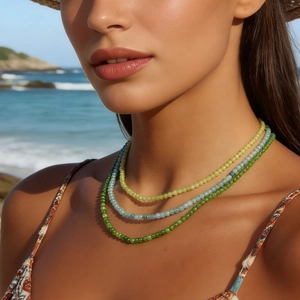 Close-up of three layered green and blue beaded necklaces on a model at the beach