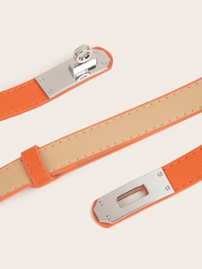 Detail of orange leather skinny belt featuring a silver polished metal turn-lock buckle
