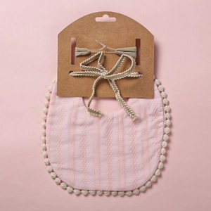 Détail du bavoir rose en gaze de coton avec bordure à pompons et bandeau assorti