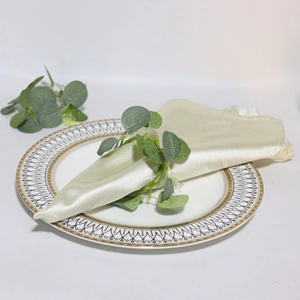 Detail of cream silk napkin with faux eucalyptus leaves on a wavy gold rim plate