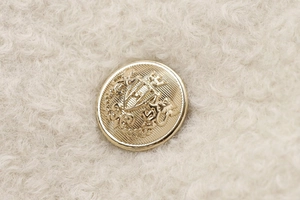 Close-up of luxury gold metal crest buttons on beige wool coat fabric detail