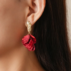 Close-up of bohemian gold studs with red acrylic petal tassels worn by a model