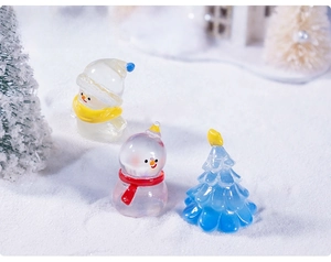 Miniature glass snowman and blue Christmas tree figurines on snow landscape background