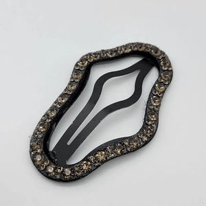 Close-up of wave-shaped black metal hair clip with sparkling brown rhinestones