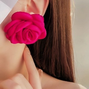 Detail shot of a large rose flower earring in vibrant rose red velvet fabric texture