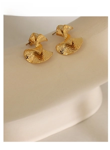 Macro shot of gold-plated fan-shaped earrings with hammered texture and retro design