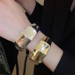Detail shot of wide metallic open cuff bracelet with fluid wavy texture in gold and silver