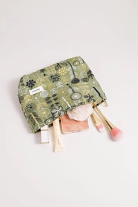 Detail of green linen makeup bag with floral embroidery and assorted cosmetics inside