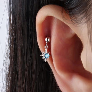 Macro view of silver star stud earring with a light blue gem worn on the ear helix
