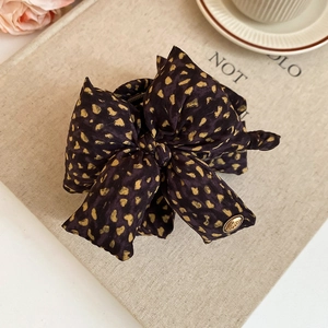 Detailed view of dark brown bow hair clip with gold dots and a small metal love charm