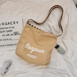 Dettaglio della borsa tote in tela kaki con stampa Bonjour e tracolla a righe tessuta