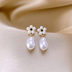 Detail of gold floral pearl earrings with black center on champagne silk background
