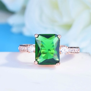 Macro shot of emerald cut green gemstone ring with rose gold band and small side diamonds
