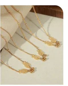 Detail view of gold fish pendants with grid textures and hanging metal beads on thin chains