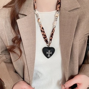 Detail of heart pendant with silver cross and leopard print strap worn by a model