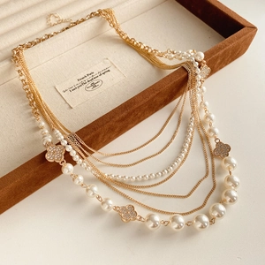 Macro detail of multi-layer gold necklace with pearls and clover charms in a velvet box