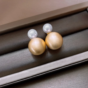 Detail view of vertical pearl and brushed gold stud earrings in a jewelry box