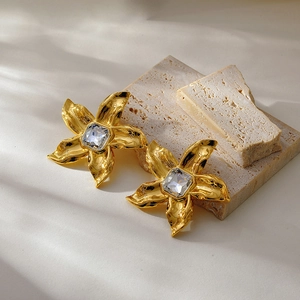 Detail of oversized gold floral earrings featuring central square crystal on stone