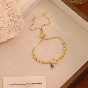 Dettaglio del bracciale a catena dorata con lettera H in pavé e ciondolo malocchio