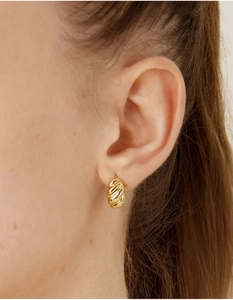Close-up of a model wearing a gold twisted huggie hoop earring with a stylish design