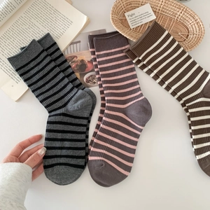 Retro striped crew socks in grey, pink, and brown knit displayed in a cozy home setting