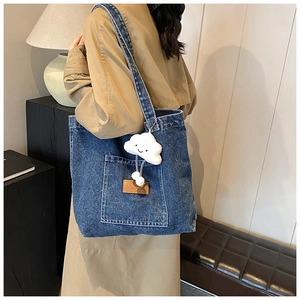 Detail of navy denim tote bag featuring a white plush cloud charm and large front pocket