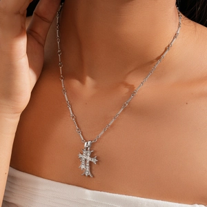 Close-up of a silver cross pendant necklace with rhinestones worn by a model