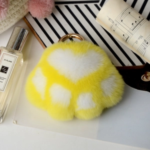 Detail view of yellow and white plush paw pendant with a golden metal ring