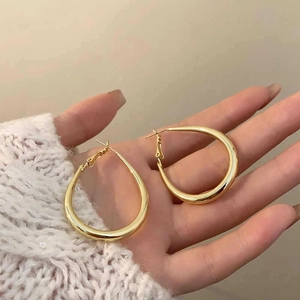Nahaufnahme von minimalistischen goldfarbenen ovalen Creolen, die in der Hand gehalten werden