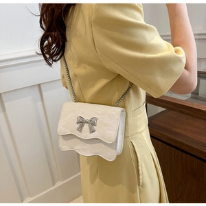 Detail shot of a white crossbody bag with silver bow accent and wavy edge design