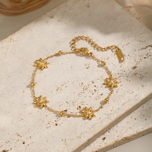 Detailed view of a gold flower bracelet with clear crystals on a natural stone surface