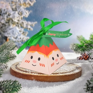 Pink pyramid Christmas candy box with cartoon elf face on snow-covered wooden base