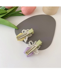 Close-up of pastel bow hair clips with white faux pearls on a light green base