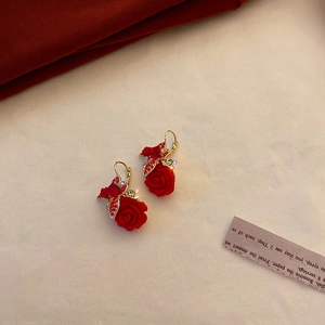 Detailed shot of red rose earrings with crystals and gold accents on a warm beige backdrop