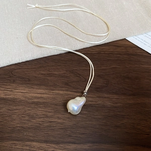 Detailed macro view of irregular baroque pearl pendant on cream-colored woven rope necklace