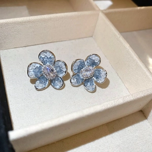 Détail de boucles d'oreilles fleurs bleues avec texture pierre et zircon central